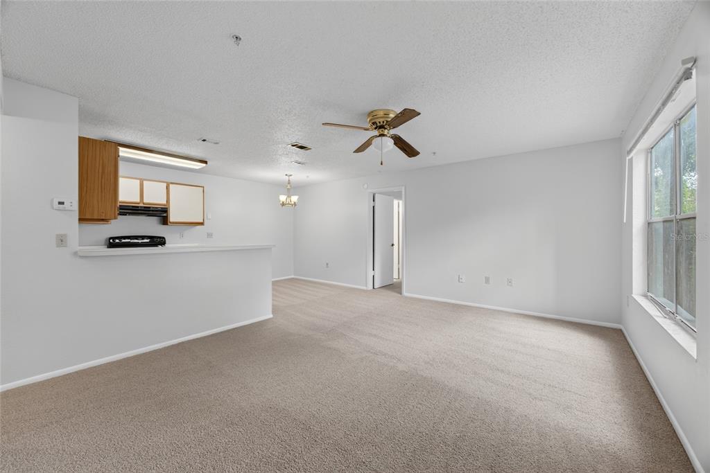 A carpeted living room with a ceiling fan opens to a kitchen with wooden cabinets — 642 DORY LANE UNIT 203, ALTAMONTE SPRINGS, FL