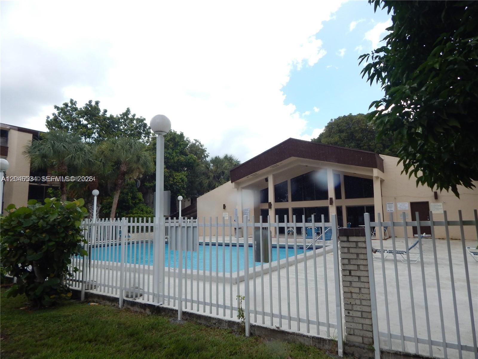A swimming pool is enclosed by a white metal fence in front of a building — 14601 N Kendall Dr # 304K, Miami FL 33186, MIAMI, FL