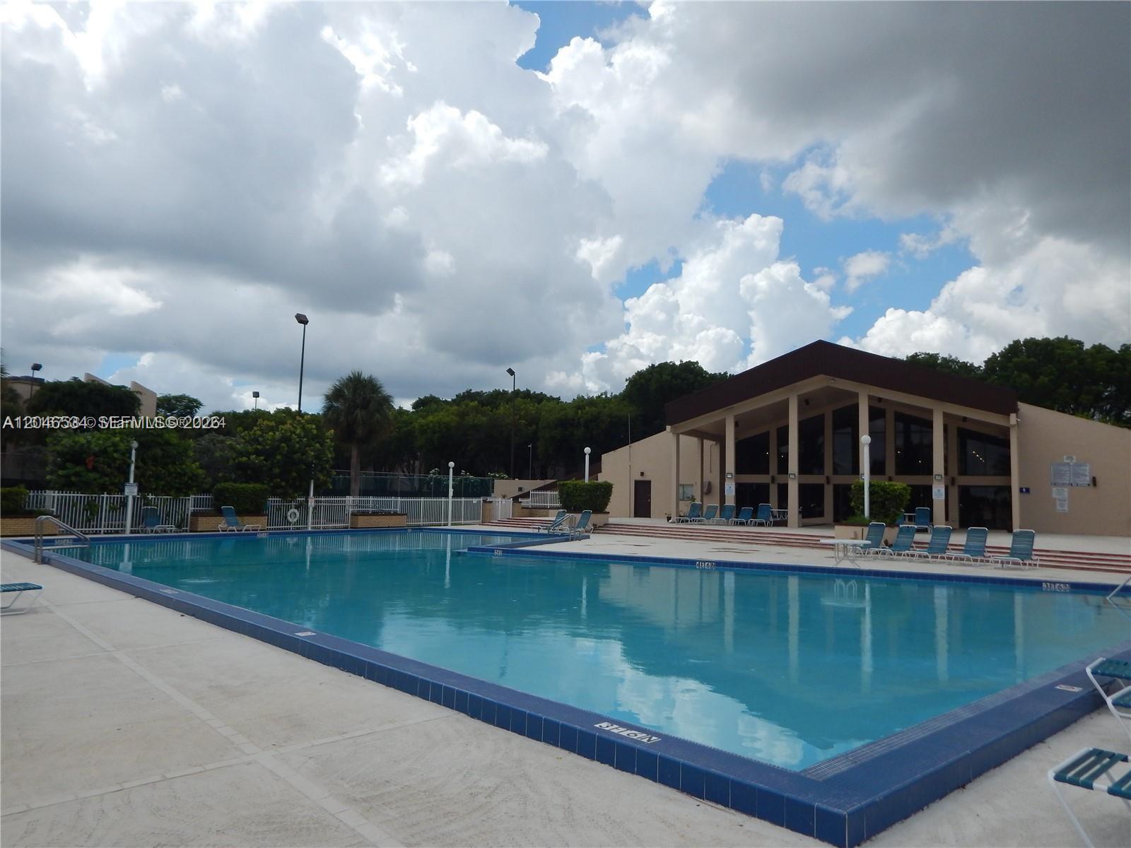 A large outdoor swimming pool sits in front of a clubhouse under a cloudy sky — 14601 N Kendall Dr # 304K, Miami FL 33186, MIAMI, FL