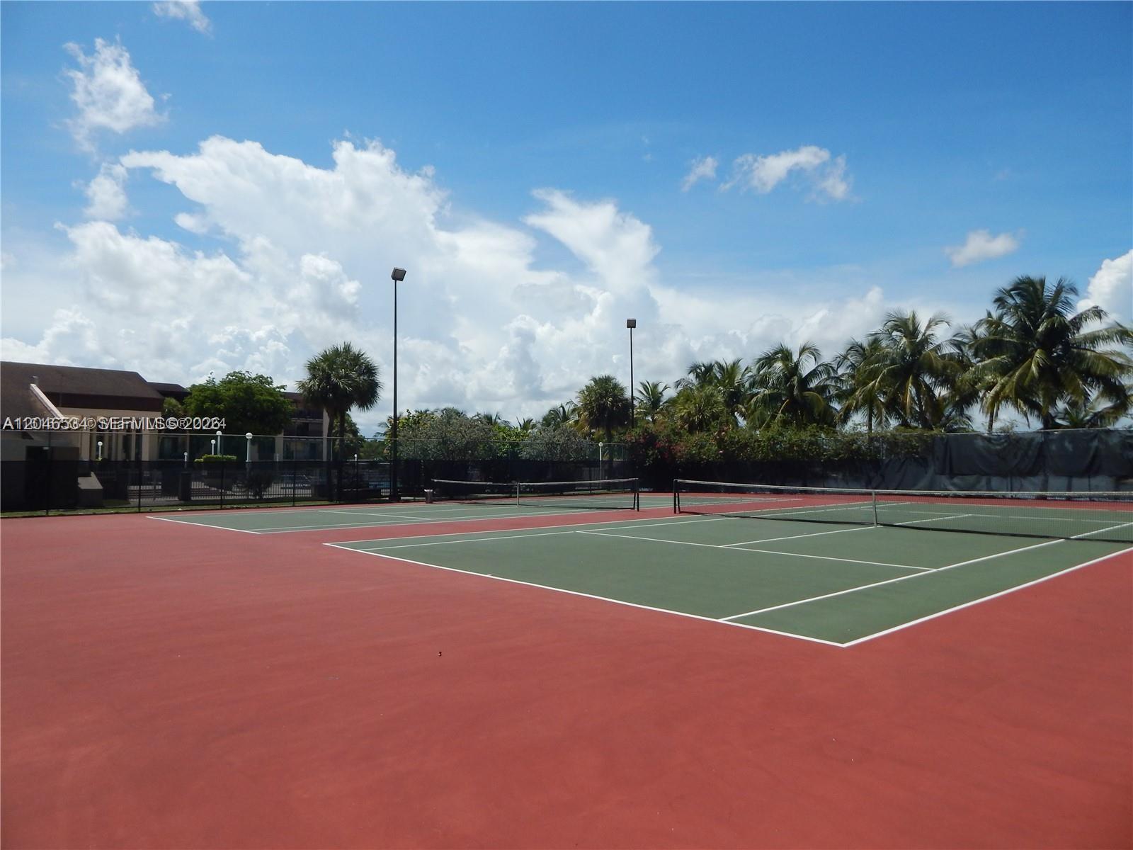 A tennis court with a green playing surface and red surrounding area under a blue sky — 14601 N Kendall Dr # 304K, Miami FL 33186, MIAMI, FL