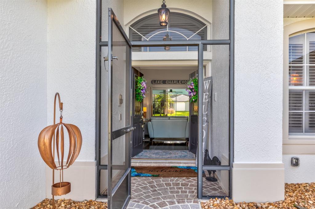 A view through an open screen door into a home entryway with a welcome sign — 5110 RIVER EDGE LANE, LEESBURG, FL