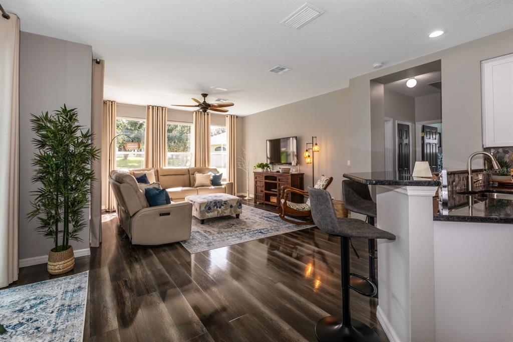 A living room with wood-look flooring, a sectional sofa, and an open kitchen breakfast bar — 5110 RIVER EDGE LANE, LEESBURG, FL
