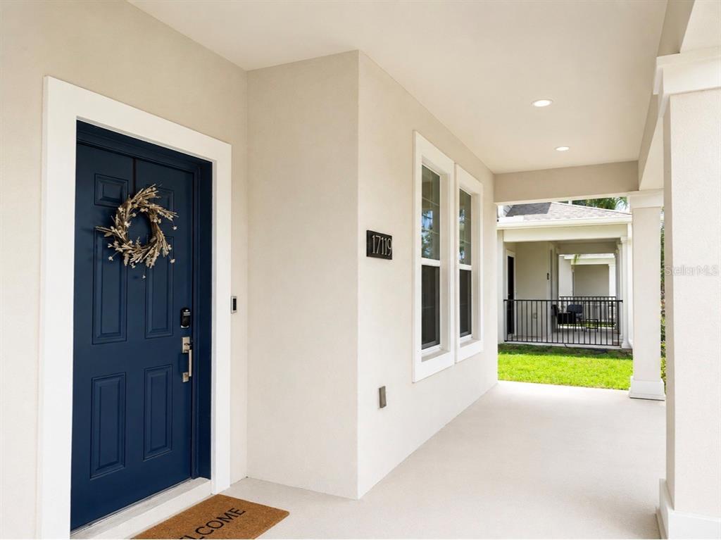 A covered front porch features a blue door with a wreath and light-colored walls — 17119 QUICKSILVER AVENUE, WINTER GARDEN, FL