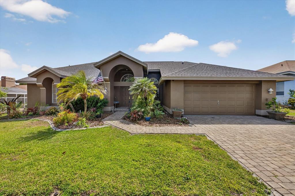 A single-story house with a brown stucco exterior, a paved driveway, and a front garden — 8687 ASHBURY DRIVE, HUDSON, FL
