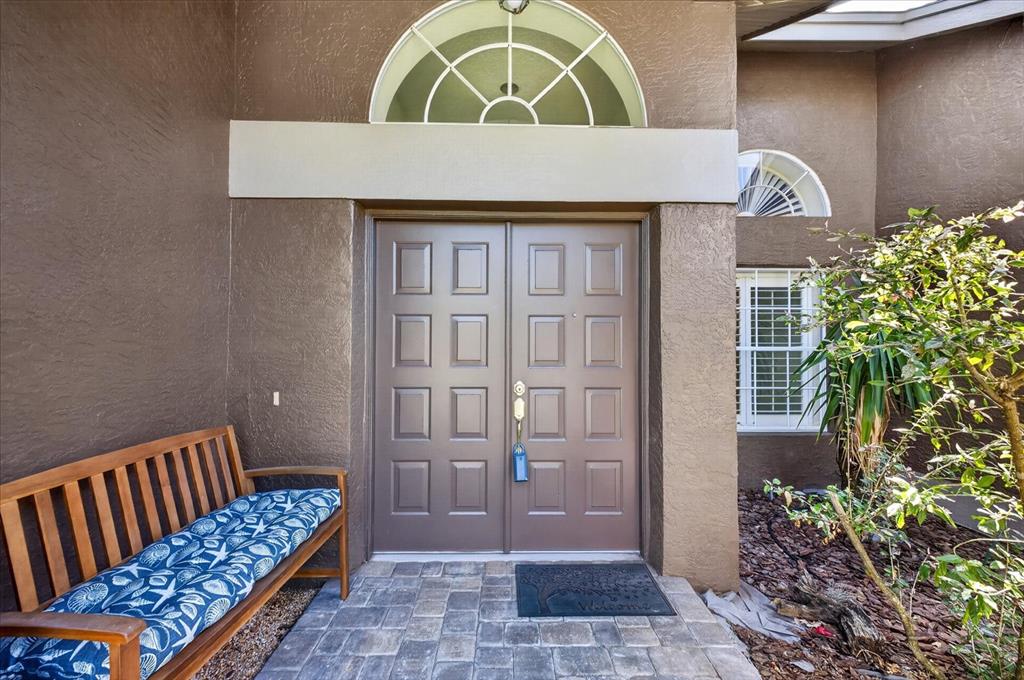 A brown double front door with a transom window and a wooden bench outside — 8687 ASHBURY DRIVE, HUDSON, FL