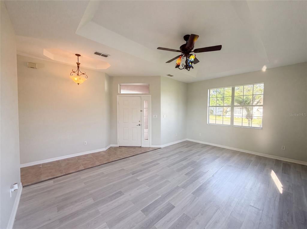 A living room with light wood-look flooring, a ceiling fan, and a tiled entryway — 204 ROUND MAN STREET, LEESBURG, FL