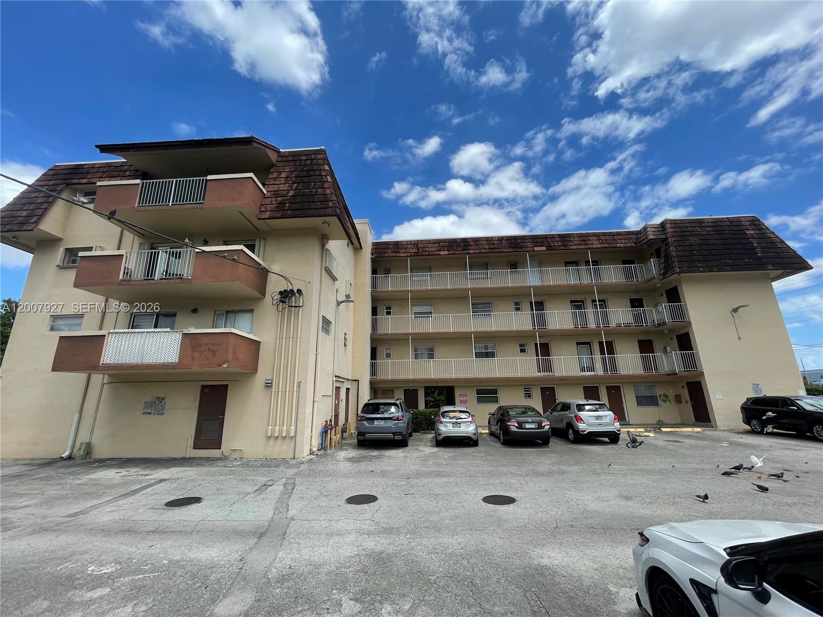 A multi-story apartment building with exterior balconies and a parking lot in front — 680 Miller Dr # W401, Miami Springs FL 33166, MIAMI SPRINGS, FL