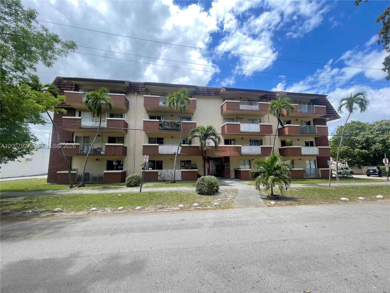 A three-story apartment building features brown balconies, palm trees, and a paved front walkway — 680 Miller Dr # W401, Miami Springs FL 33166, MIAMI SPRINGS, FL