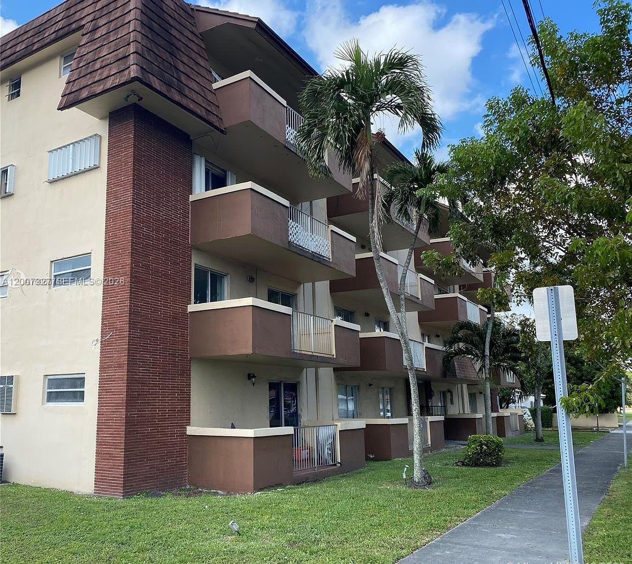 A multi-story apartment building features brown brick accents, balconies, and a palm tree — 680 Miller Dr # W401, Miami Springs FL 33166, MIAMI SPRINGS, FL