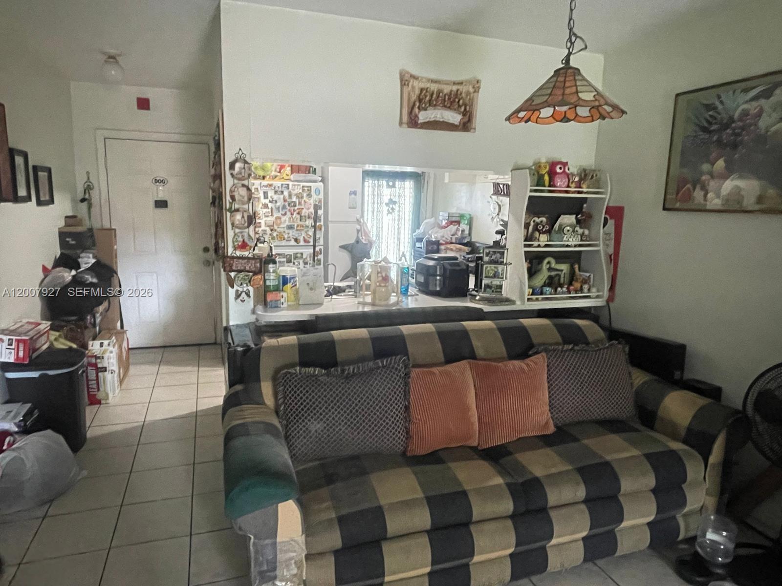 A living room features a plaid sofa, a pass-through kitchen counter, and a hanging lamp — 680 Miller Dr # W401, Miami Springs FL 33166, MIAMI SPRINGS, FL