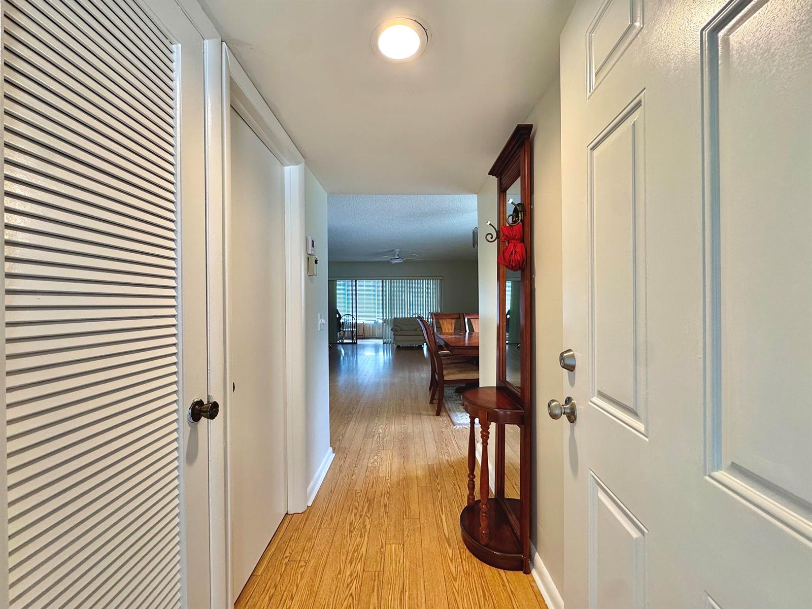 A hallway with light wood flooring leads from an entryway toward a dining area — 565 Piedmont L, Delray Beach FL 33484, DELRAY BEACH, FL