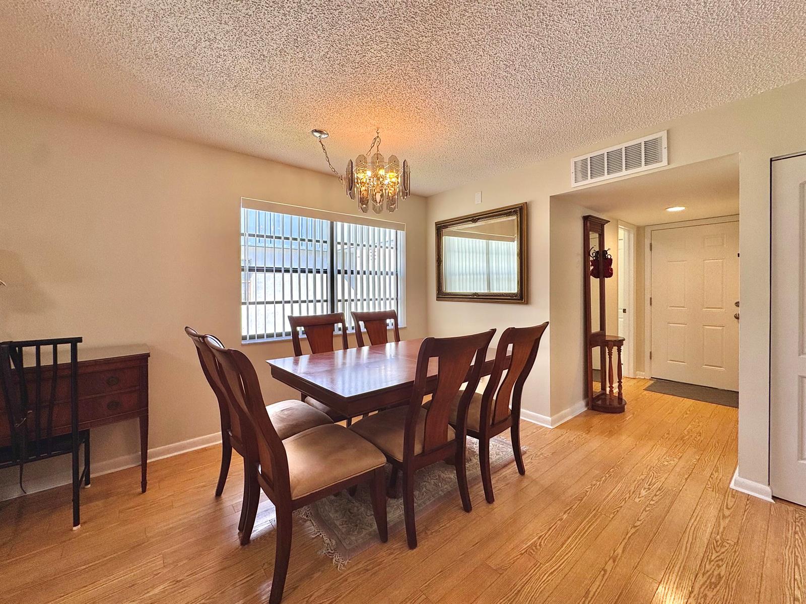 A dining room features a wooden table, six chairs, a chandelier, and hardwood flooring — 565 Piedmont L, Delray Beach FL 33484, DELRAY BEACH, FL