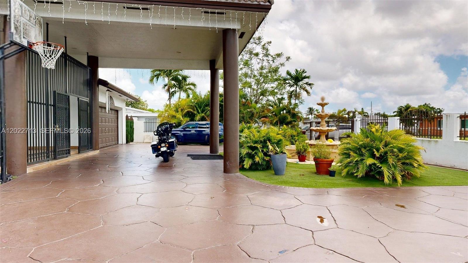 A paved driveway features a motorcycle, a tiered fountain, and a basketball hoop under a portico — 357 W 44th St, Hialeah FL 33012, HIALEAH, FL