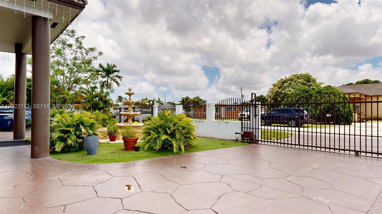 A paved driveway leads to a gated entrance with a fountain and tropical landscaping — 357 W 44th St, Hialeah FL 33012, HIALEAH, FL