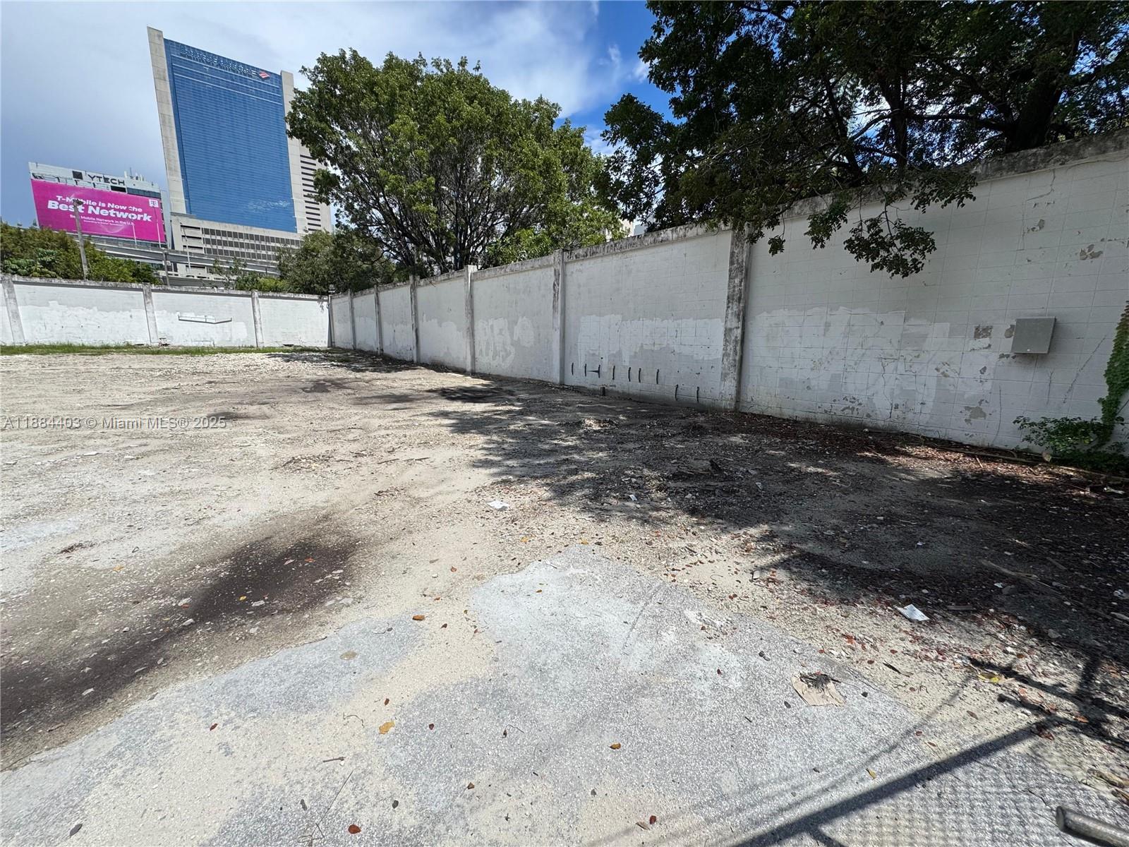 A vacant, dirt-covered lot is enclosed by a long, weathered white concrete block wall — 201 SE 2nd Ave, Miami FL 33131, MIAMI, FL