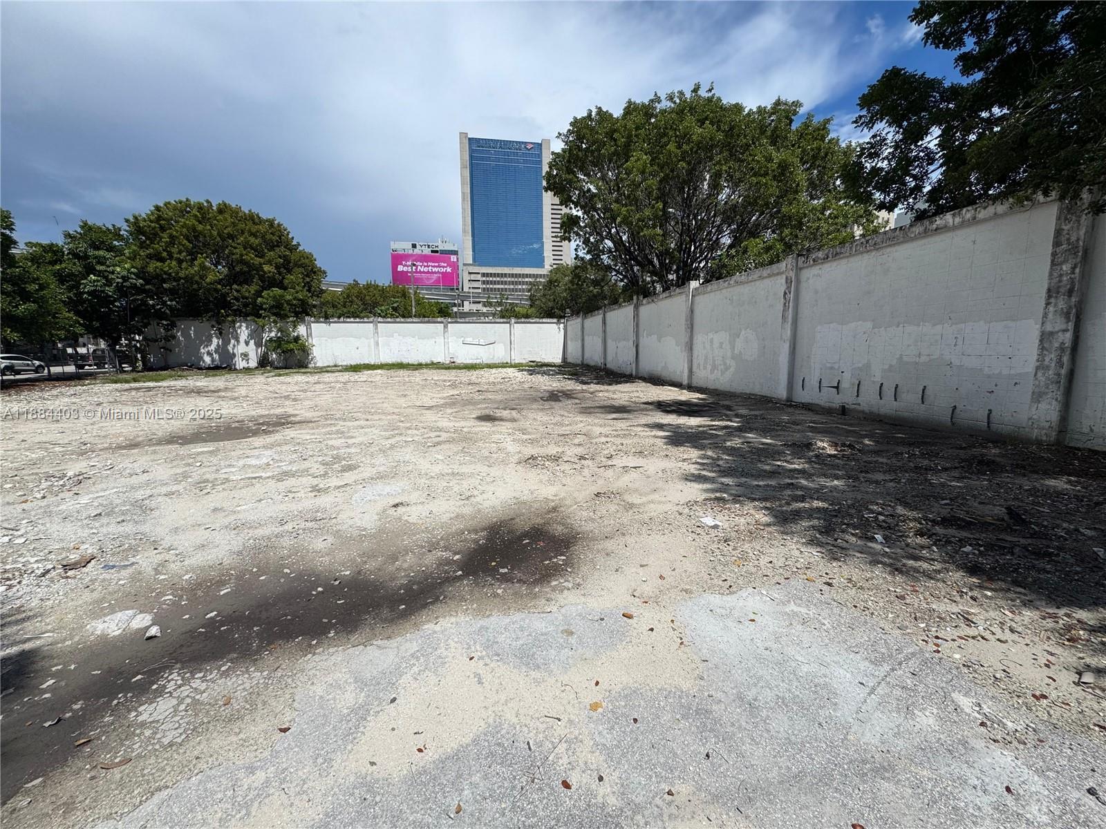 An empty, dirt-covered vacant lot is enclosed by a tall white concrete perimeter wall — 201 SE 2nd Ave, Miami FL 33131, MIAMI, FL