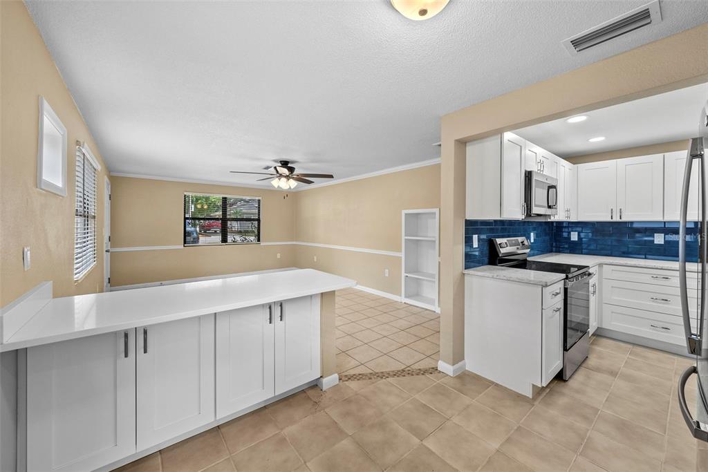 A kitchen with white cabinets and blue tile backsplash opens into a dining area — 1193 & 1195 BASS BOULEVARD, DUNEDIN, FL