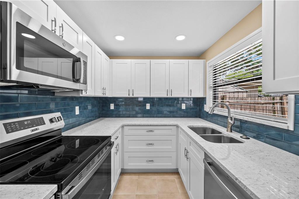 A kitchen features white cabinets, a blue subway tile backsplash, and light-colored stone countertops — 1193 & 1195 BASS BOULEVARD, DUNEDIN, FL