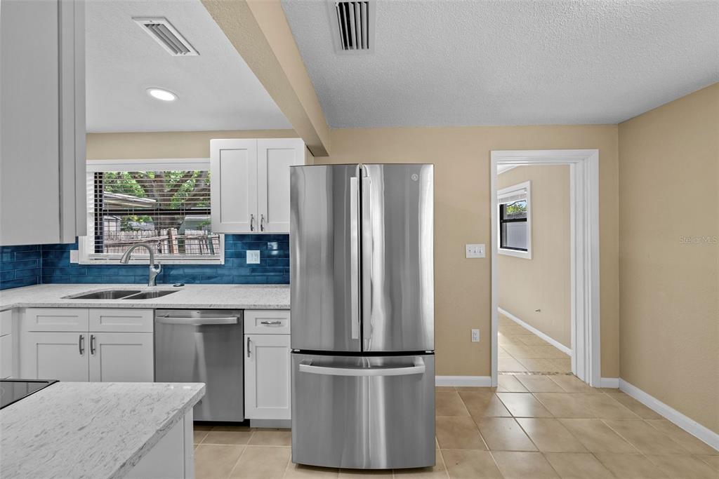 A kitchen features white cabinets, a stainless steel refrigerator, and a blue tiled backsplash — 1193 & 1195 BASS BOULEVARD, DUNEDIN, FL
