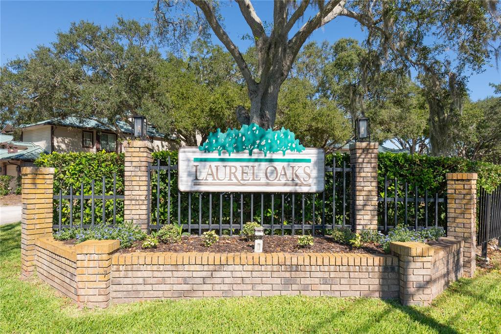 A brick entrance sign for Laurel Oaks stands in front of trees and a fence — 1471 MAHOGANY LANE UNIT 1706, PALM HARBOR, FL