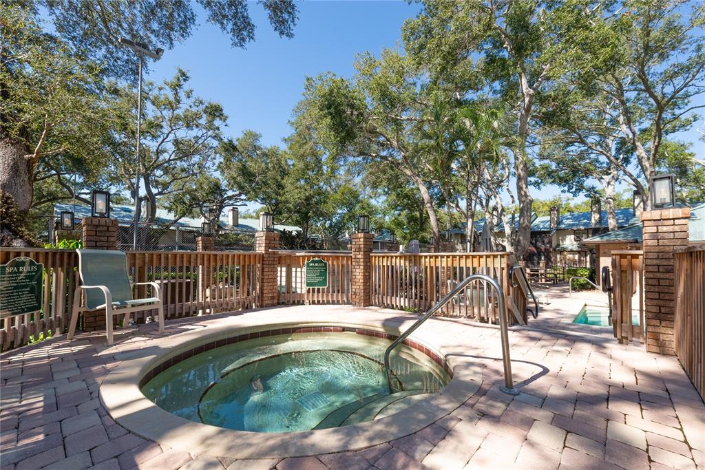 An outdoor hot tub is surrounded by a brick patio, wooden fencing, and mature trees — 1471 MAHOGANY LANE UNIT 1706, PALM HARBOR, FL
