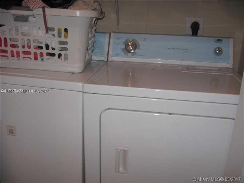 A white clothes dryer sits next to a washing machine with a laundry basket on top — 2071 Renaissance Blvd # 305, Miramar FL 33025, MIRAMAR, FL