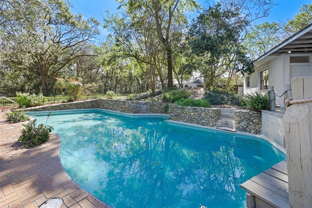 A backyard swimming pool features a stone retaining wall, brick patio, and surrounding mature trees — 2830 SE 31ST STREET, OCALA, FL
