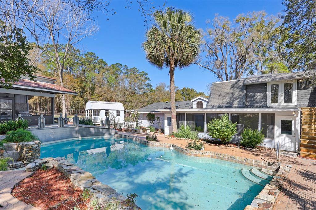 A backyard swimming pool with stone coping sits in front of a house and shed — 2830 SE 31ST STREET, OCALA, FL