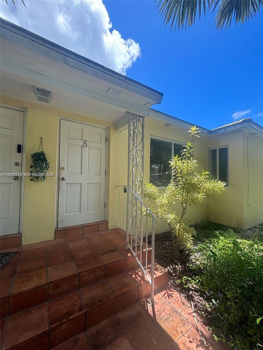 A yellow exterior wall features a white door, tiled steps, and a decorative metal railing — 1015 NE 112th St, Biscayne Park FL 33161, BISCAYNE PARK, FL