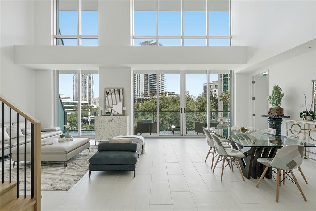 A modern, high-ceilinged living and dining area with white tile floors and floor-to-ceiling windows — 400 CENTRAL AVENUE UNIT 303, ST PETERSBURG, FL