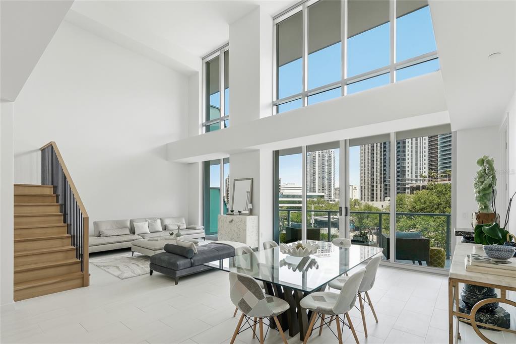 A modern living and dining area features double-height ceilings, floor-to-ceiling windows, and a wooden staircase — 400 CENTRAL AVENUE UNIT 303, ST PETERSBURG, FL