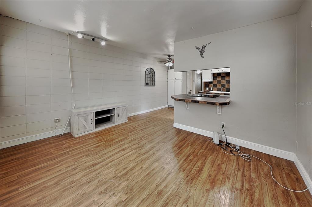 A living room with wood-look flooring, a block wall, and a pass-through to the kitchen — 313 S LAWSONA BOULEVARD, ORLANDO, FL