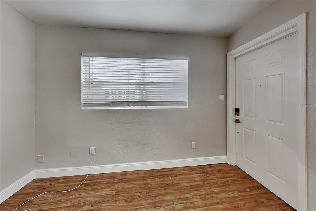 A room with light gray walls, wood-look flooring, a window with blinds, and a white door — 313 S LAWSONA BOULEVARD, ORLANDO, FL