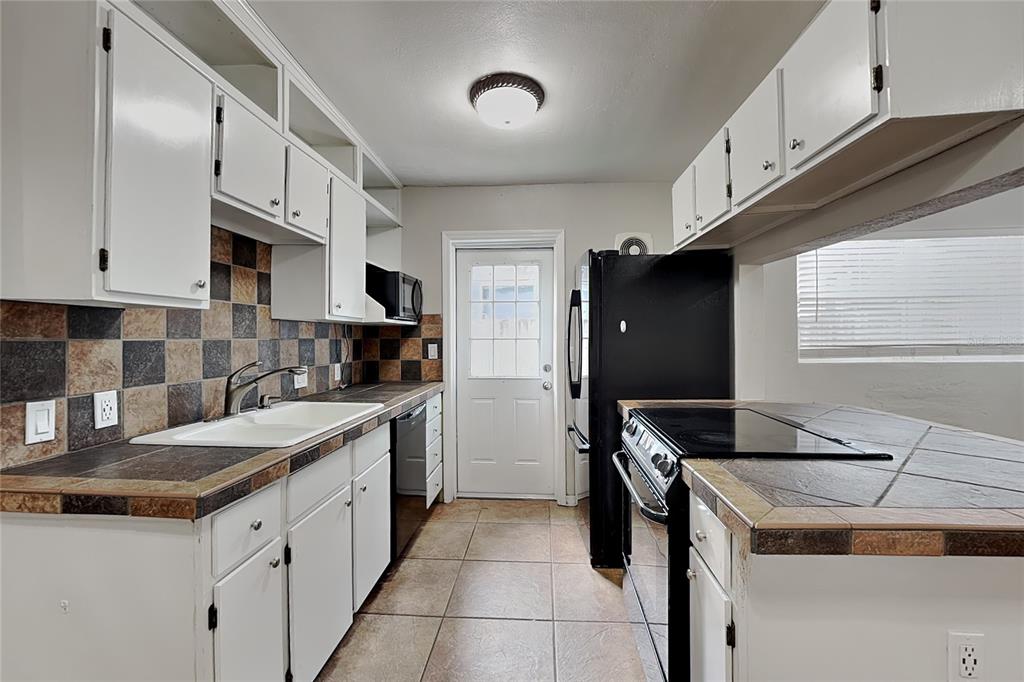 A galley kitchen features white cabinets, tiled countertops, a black refrigerator, and a back door — 313 S LAWSONA BOULEVARD, ORLANDO, FL