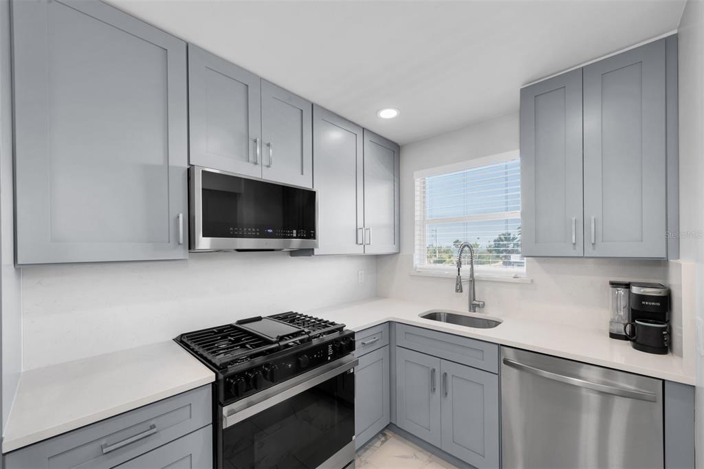 A modern kitchen features light blue cabinets, stainless steel appliances, and white quartz countertops — 3128 59TH STREET S UNIT 303, GULFPORT, FL