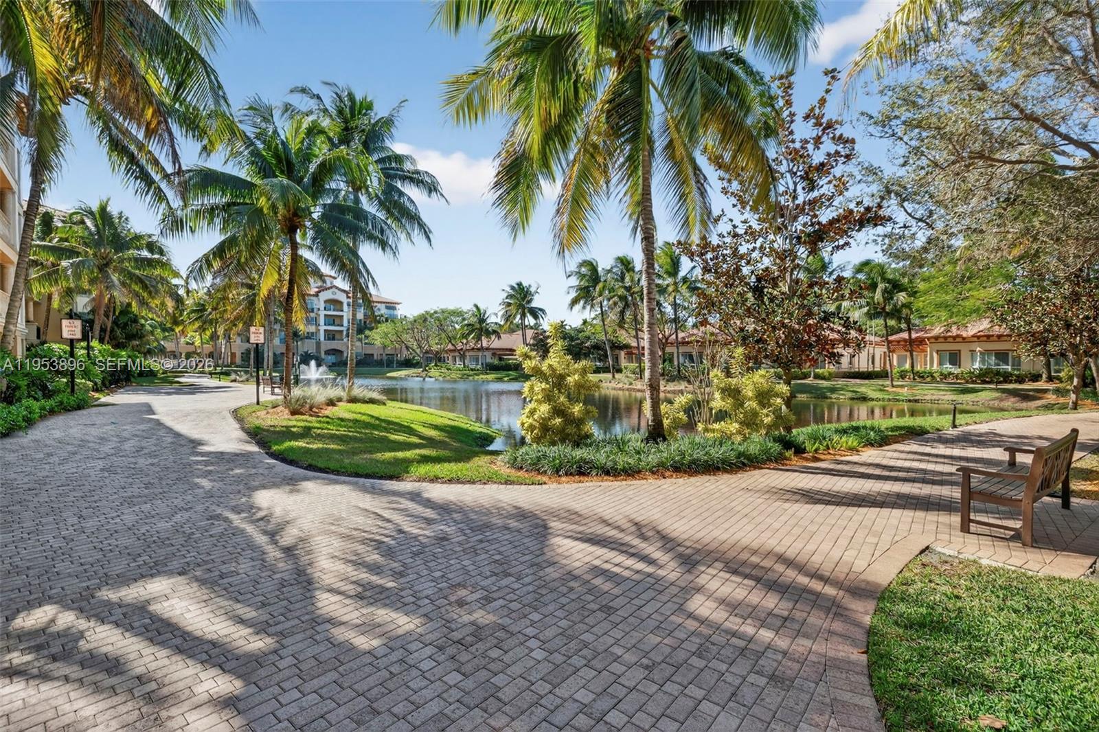 A paved walkway winds past a pond and palm trees toward residential buildings — 16135 Emerald Estates Dr # 162, Weston FL 33331, WESTON, FL