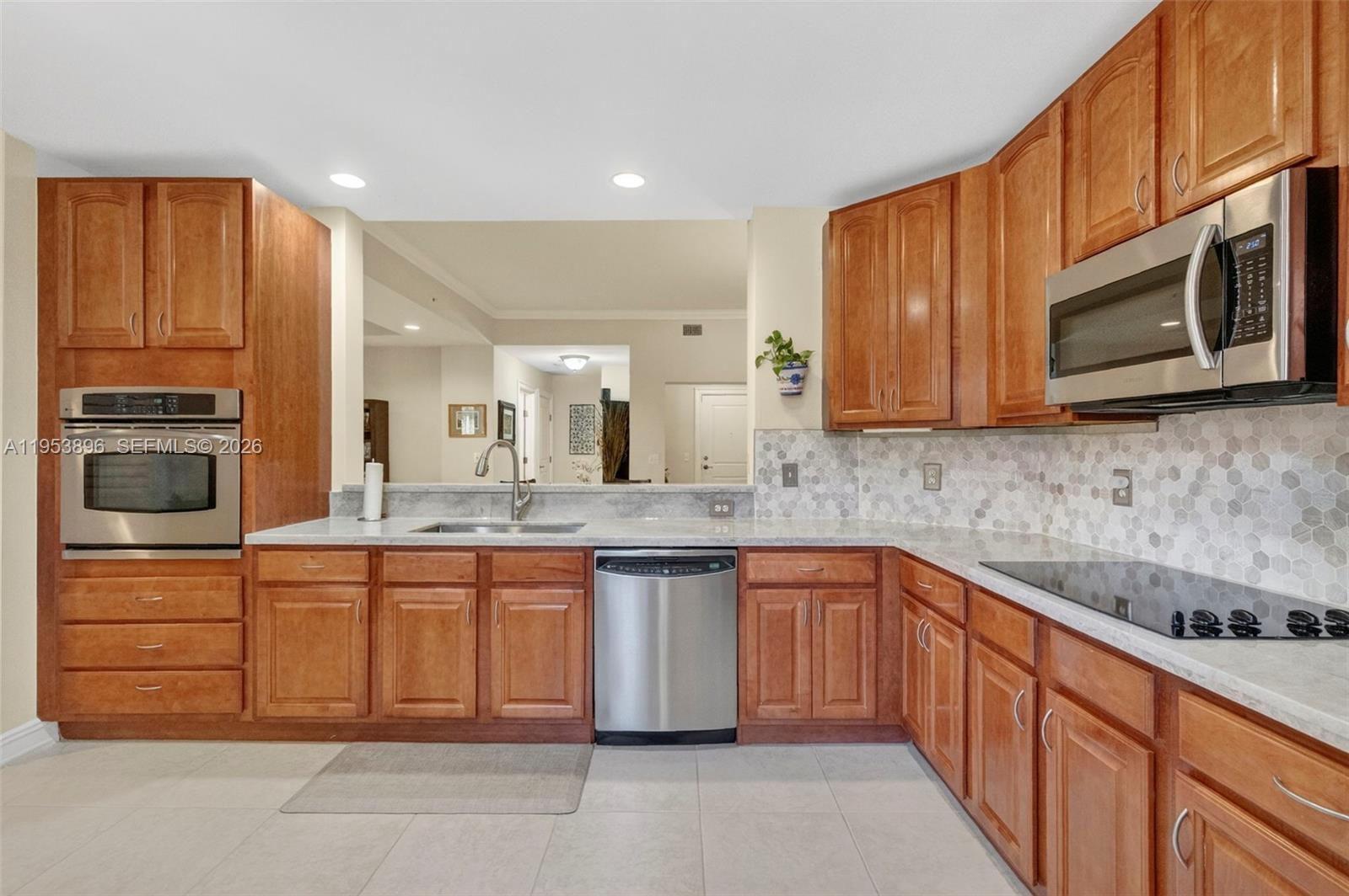 A kitchen features wood cabinets, stainless steel appliances, and a light-colored hexagonal tile backsplash — 16135 Emerald Estates Dr # 162, Weston FL 33331, WESTON, FL