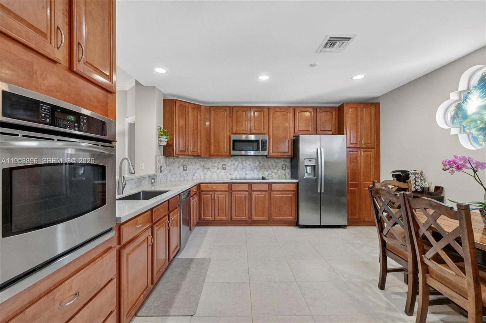 A kitchen features wood cabinets, stainless steel appliances, light countertops, and a dining area — 16135 Emerald Estates Dr # 162, Weston FL 33331, WESTON, FL