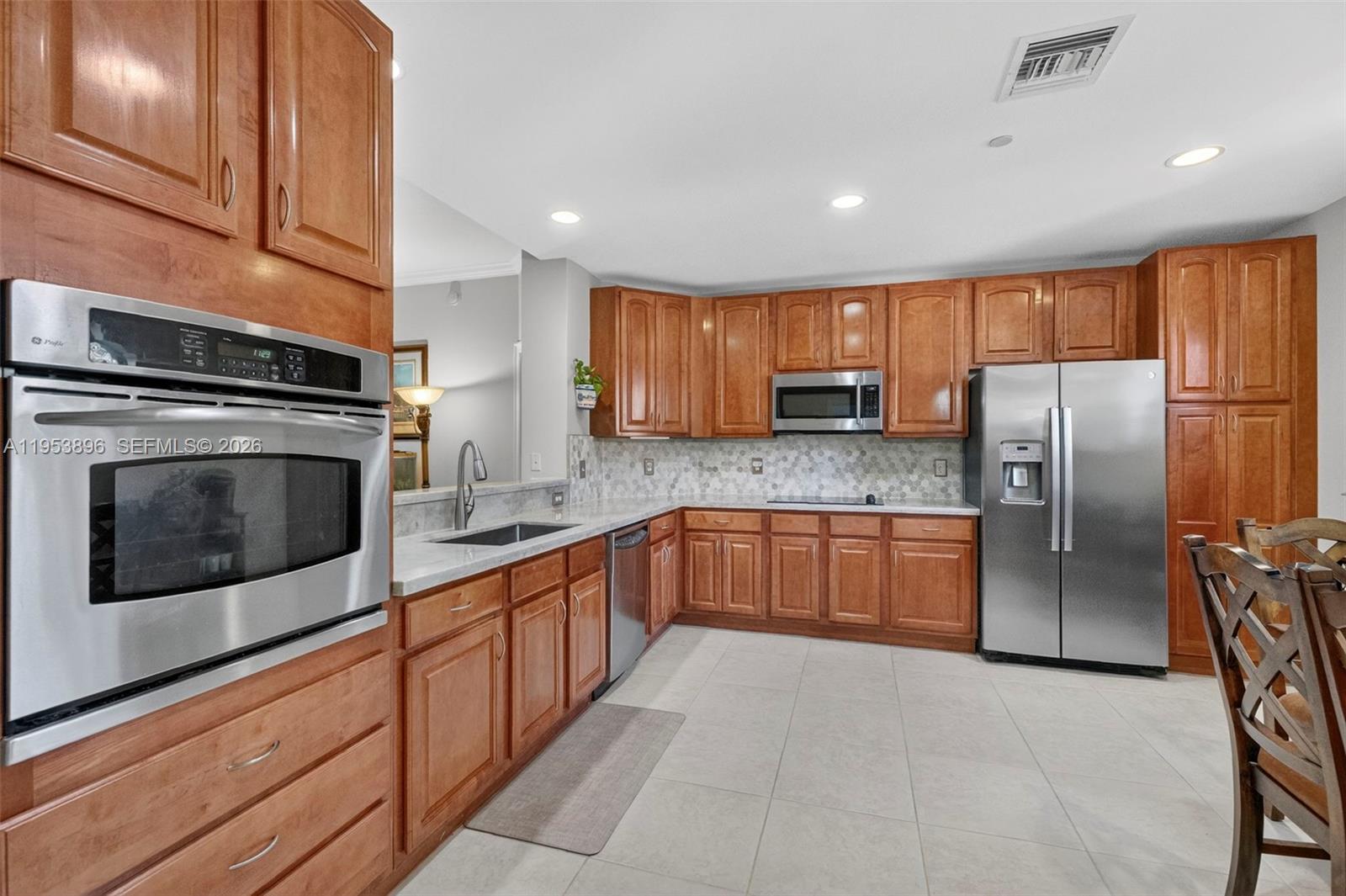 A kitchen features wood cabinets, stainless steel appliances, a tiled backsplash, and light-colored floor tiles — 16135 Emerald Estates Dr # 162, Weston FL 33331, WESTON, FL