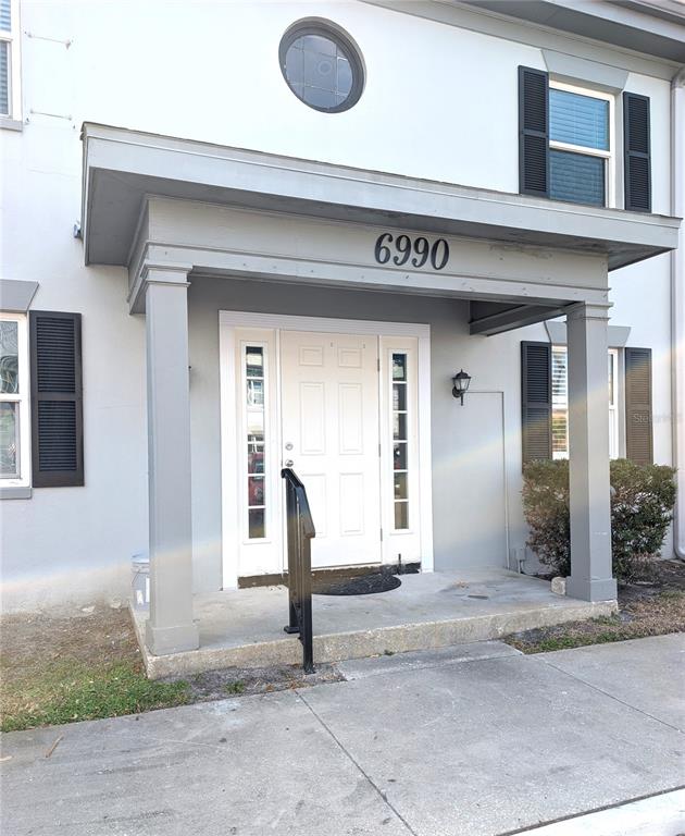 The exterior of a light gray building features a covered porch with a white door — 6990 PLACE DE LA PAIX UNIT 1A, SOUTH PASADENA, FL