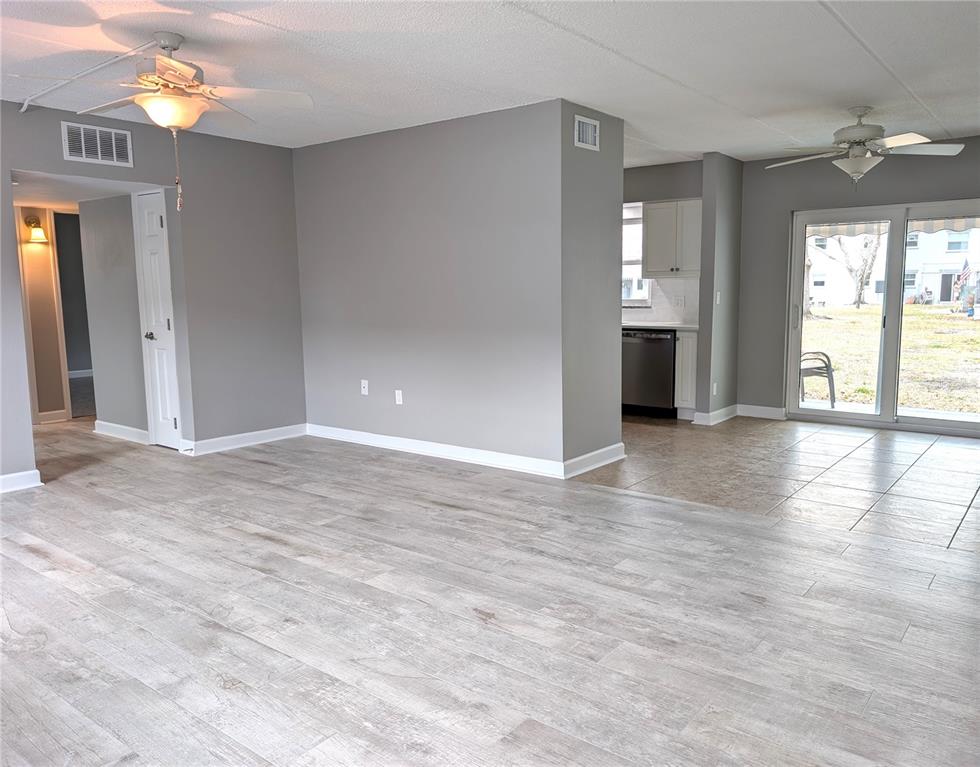 An open-concept living area features light wood-look flooring, gray walls, and a sliding glass door — 6990 PLACE DE LA PAIX UNIT 1A, SOUTH PASADENA, FL