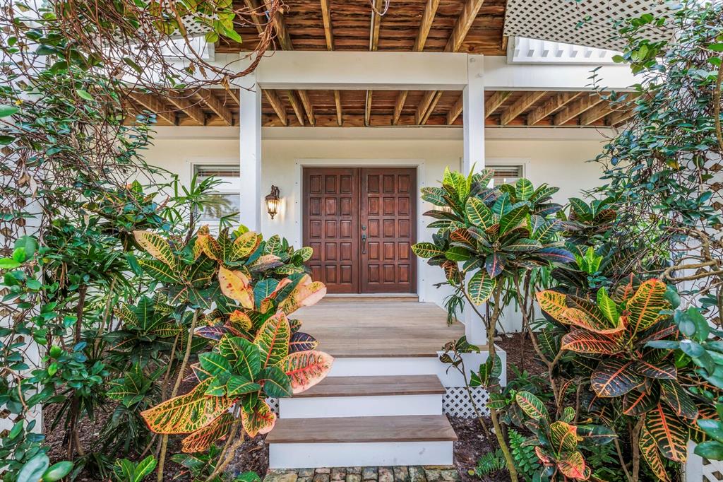 A wooden front porch with double doors is framed by lush tropical plants and stairs — 1678 JOSE GASPAR DRIVE, BOCA GRANDE, FL