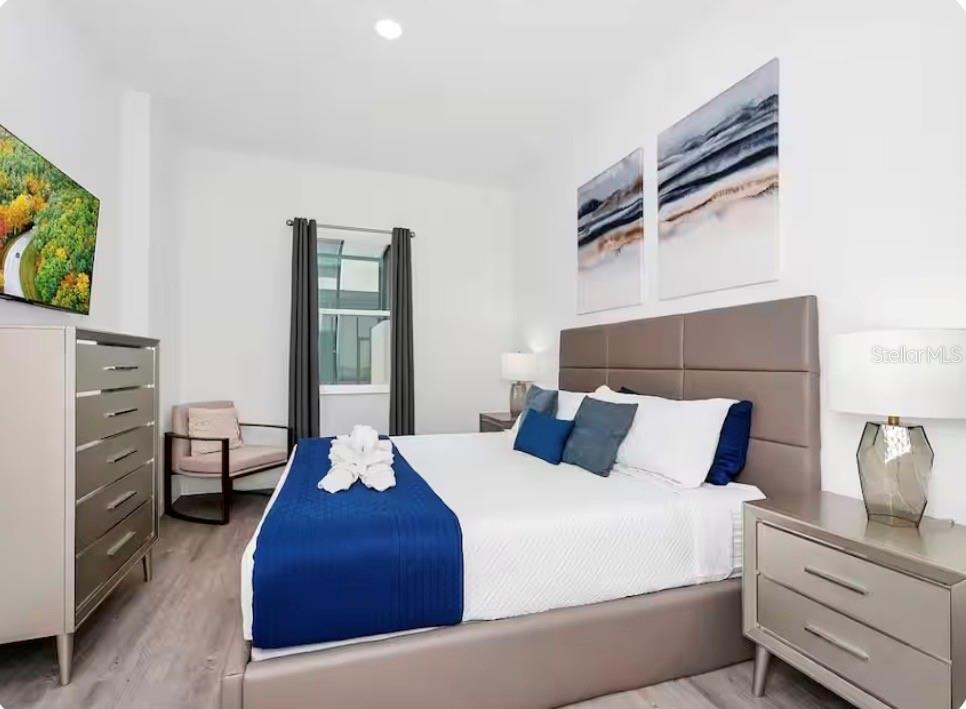 A modern bedroom features a king bed, gray furniture, wood-look flooring, and wall-mounted artwork — 363 FAMAGUSTA DRIVE, DAVENPORT, FL