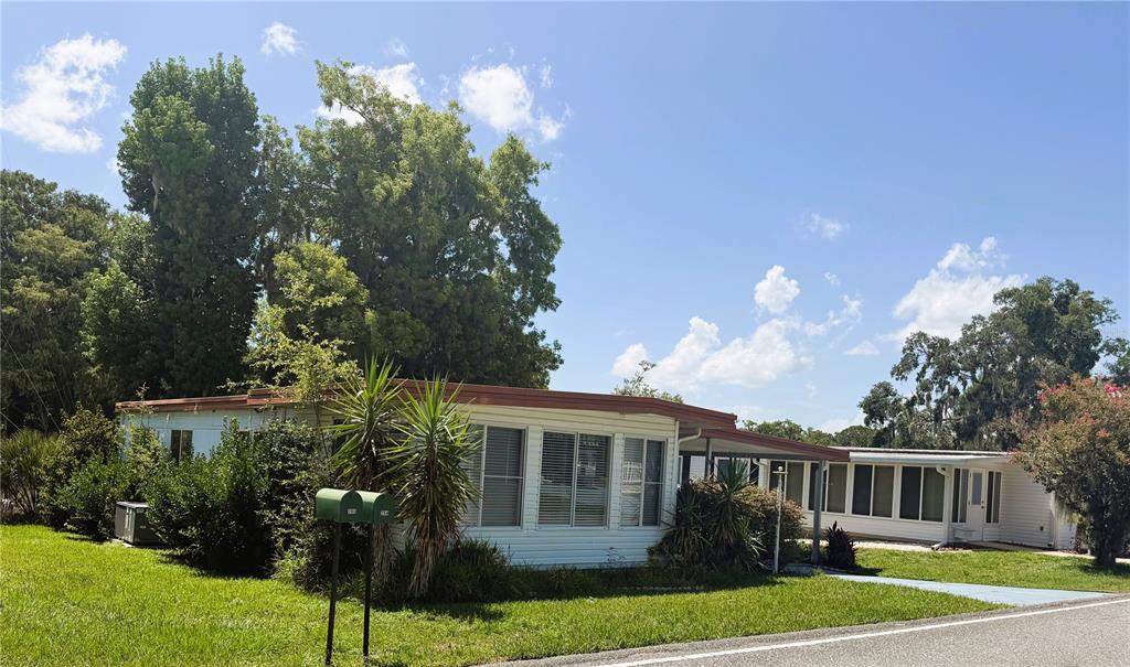 A single-story mobile home with white siding and a carport sits on a grassy lot — 203 ASPEN CIRCLE, LEESBURG, FL