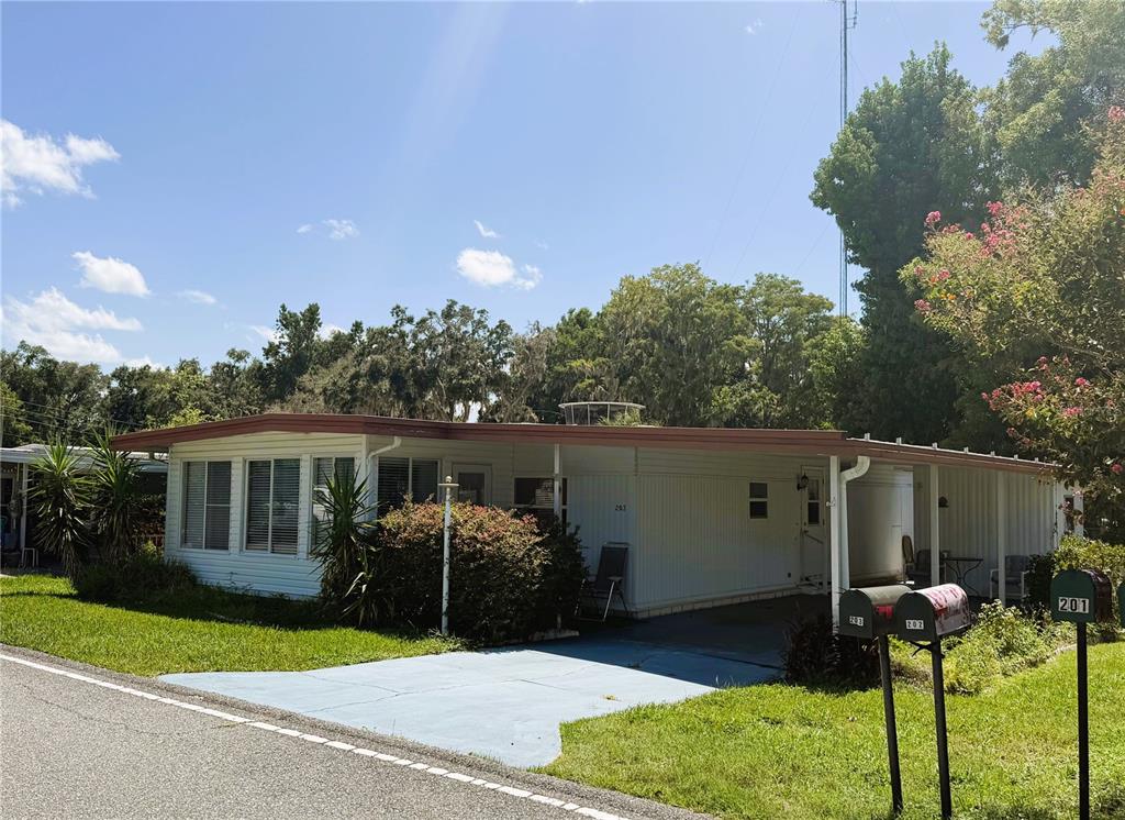 A single-story manufactured home with a carport and two mailboxes sits beside a road — 203 ASPEN CIRCLE, LEESBURG, FL
