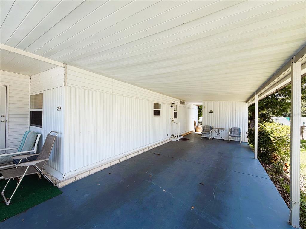 A covered carport with a concrete floor sits beside a white mobile home — 203 ASPEN CIRCLE, LEESBURG, FL