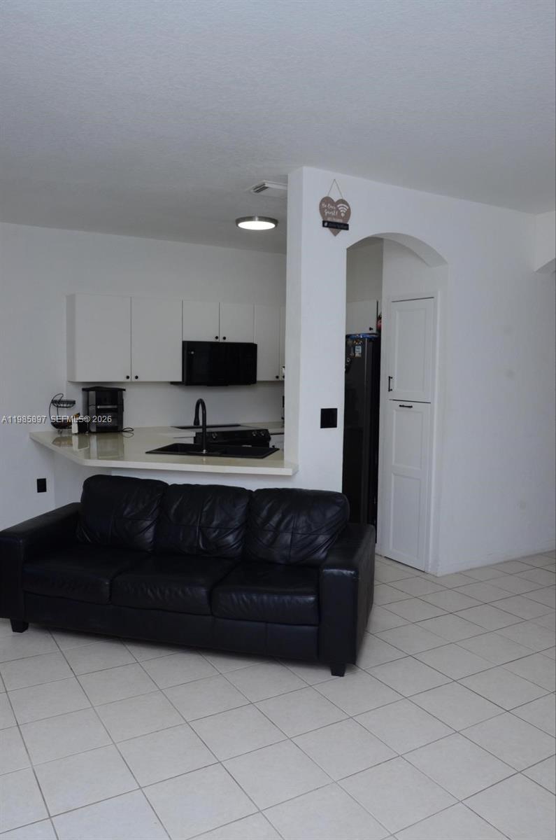 A black leather sofa sits in front of a kitchen with white cabinets and counters — 12505 SW 124th Ct, Miami FL 33186, MIAMI, FL