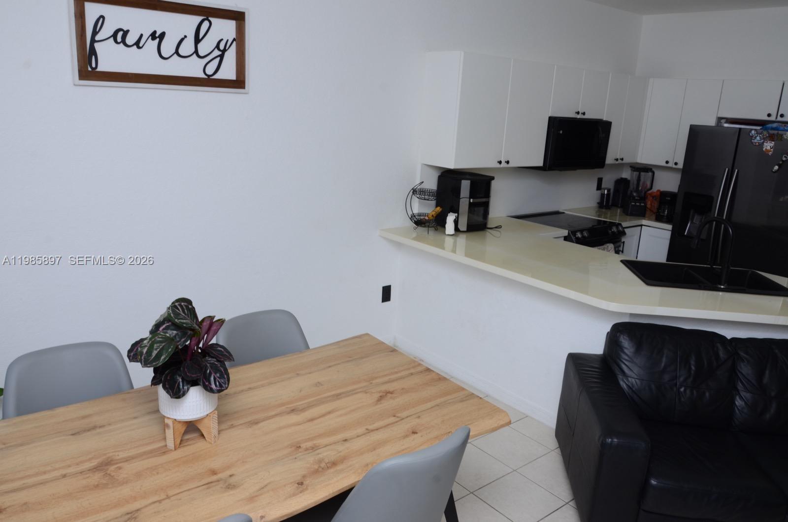 A dining area with a wooden table sits adjacent to a kitchen with white cabinets — 12505 SW 124th Ct, Miami FL 33186, MIAMI, FL