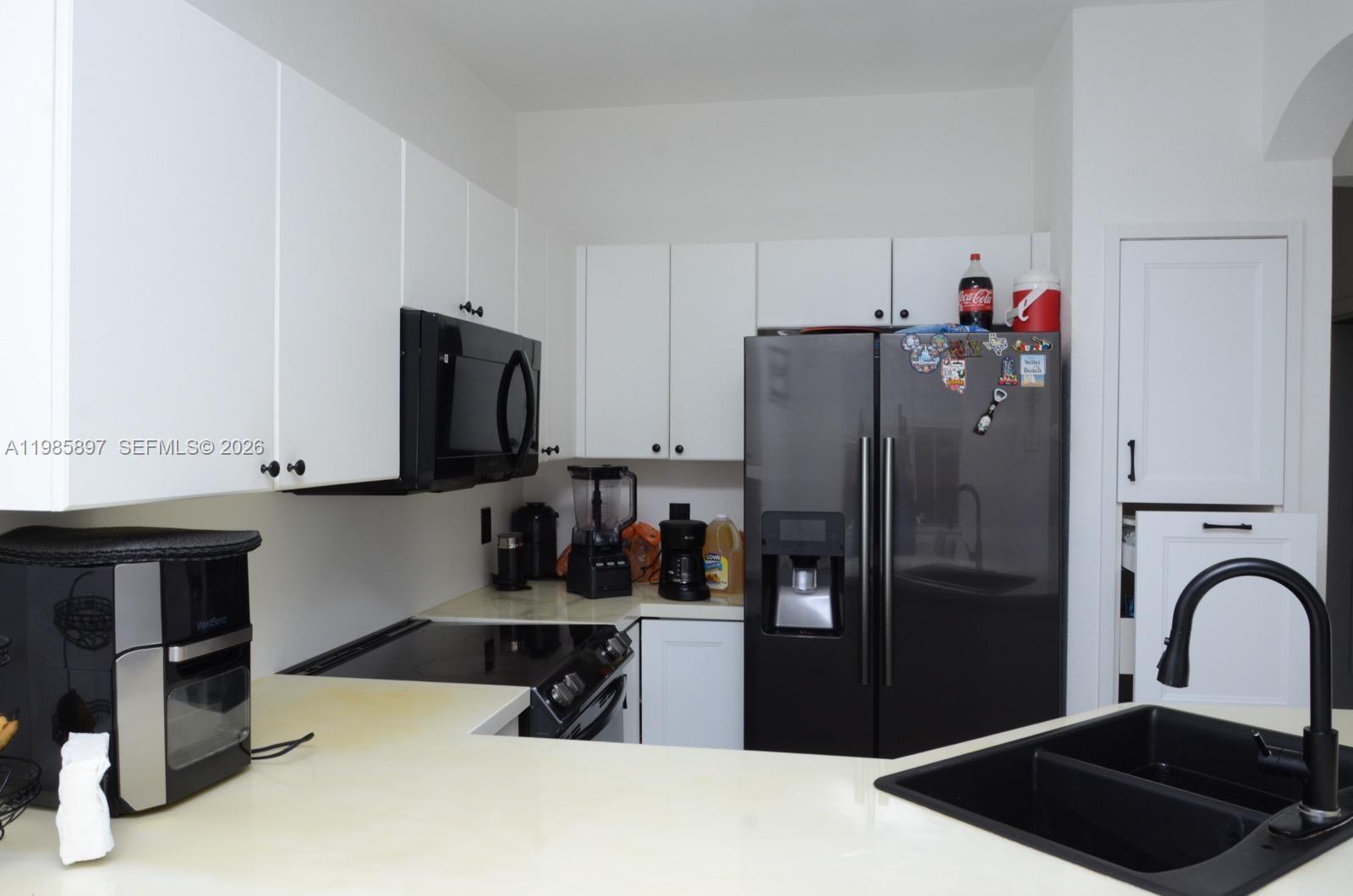 A kitchen features white cabinets, black appliances, a black sink, and light-colored countertops — 12505 SW 124th Ct, Miami FL 33186, MIAMI, FL