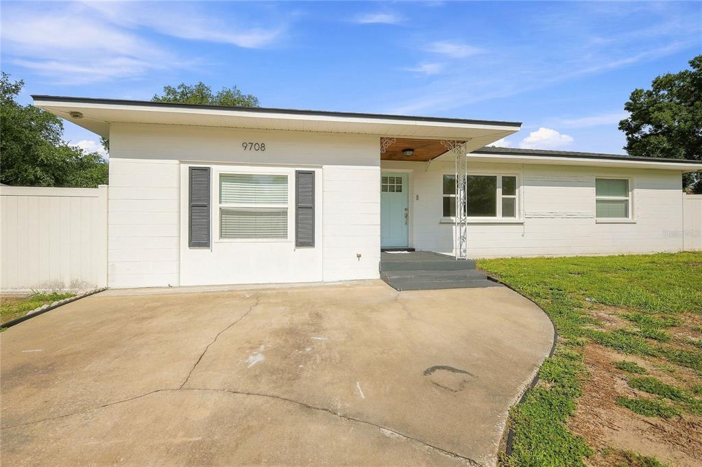A single-story house with a white exterior, a concrete driveway, and a light blue door — 9708 FOREST HILLS DRIVE, TAMPA, FL